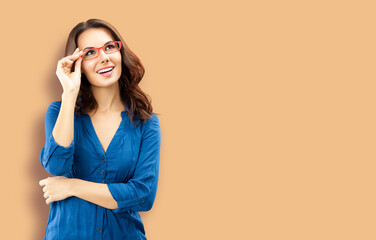 Portrait of happy smiling brunette woman looking up, in red eye glasses, blue confident wear, isolated latte beige background. Business studio concept. Copy space area for text.