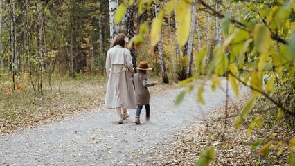 Hello September. A young mother and little daughter walk in the city park in autumn.