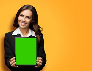 Portrait of happy smiling brunette businesswoman showing tablet pc, touchpad, with copy space for text, isolated against vivid orange background. Confident beautiful young business woman at studio