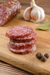 Salami sausage cut slices and salami sausage half with bay leaf, garlic and pepper on cutting board