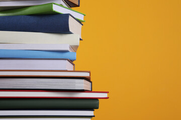 Stack of hardcover books on orange background, closeup. Space for text