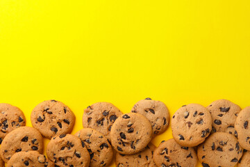 Many delicious chocolate chip cookies on yellow background, flat lay. Space for text