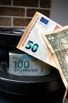 Russian 100 rubles, 50 euros, and dollars on top of each other with a weight behind, vertical shot