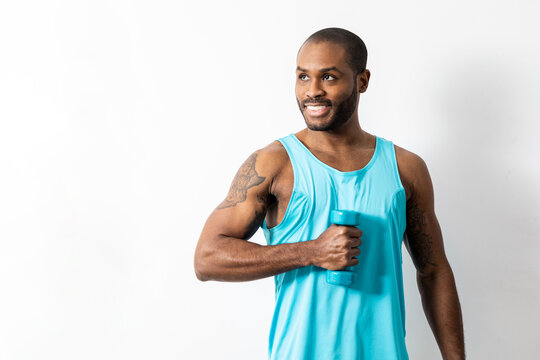 Muscular dark-skinned man poses on a white background in sportswear with suspenders. The adult lifts a small dumbbell with the biceps.Concept of bodybuilding in African men.
