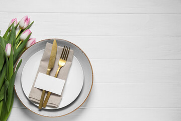 Stylish table setting with cutlery, paper card and tulips on white wooden background, flat lay. Space for text