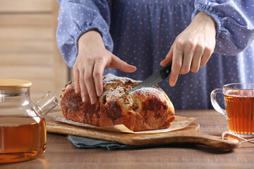 Woman cutting delicious yeast dough cake at wooden table, closeup