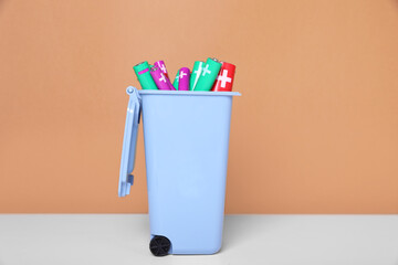 Many used batteries in recycling bin on white table against light brown background