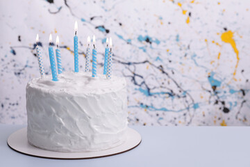 Delicious cake with cream and burning candles on light blue table. Space for text