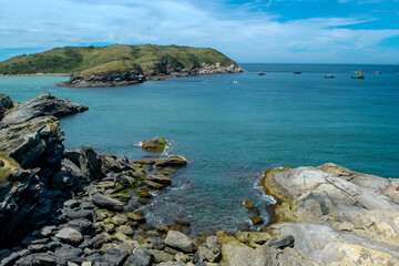 The beautiful beach at Forte São Mateus in Cabo Frio at the end of the afternoon, with many mountains around and rocks with sea water around them.