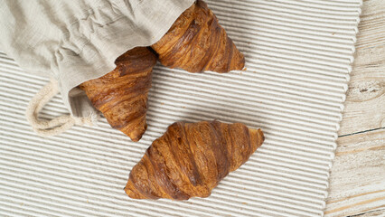 Croissants in eco bag on wooden table. Eco-friendly linen bag with fresh croissants.