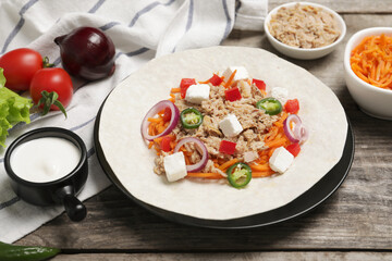 Delicious tortilla with tuna, vegetables and cheese on wooden table. Cooking shawarma