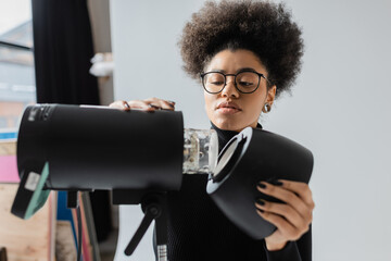african american content maker in eyeglasses assembling strobe spotlight in photo studio.