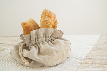Organic ciabatta packaged in a reusable linen bread bag, placed on a wooden table adorned with a delightful tablecloth.