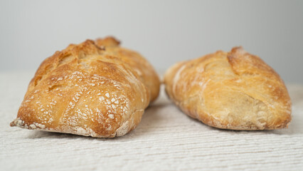 Freshly baked ciabatta on a white table. Two rustic ciabattas resting on a minimalist white surface.