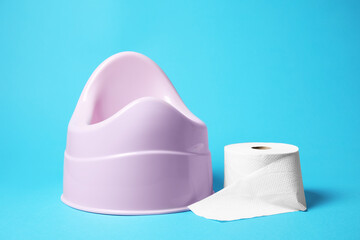 Pink baby potty and toilet paper on light blue background