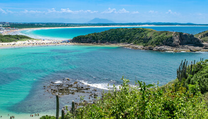 Top view of Praia das Conchas, close to the city of Cabo Frio, with white sand beaches, blue sky, sea with clean waters and in shades of green and blue, with mountains in the background.