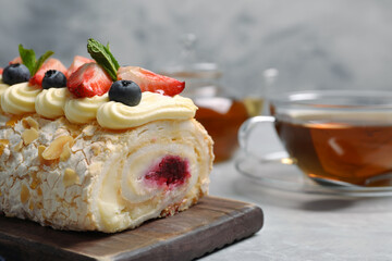 Tasty meringue roll with jam, cream, strawberry, blueberry and mint on light grey table, closeup. Space for text