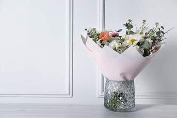 Bouquet of beautiful flowers in vase on wooden table against white wall. Space for text