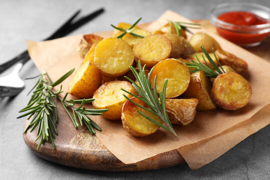Tasty baked potato and aromatic rosemary served on wooden board, closeup