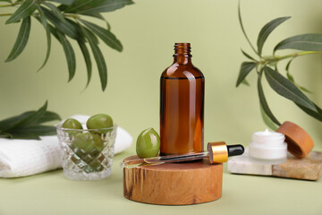 Glass bottle of serum and olives on green background
