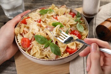 Woman eating delicious pasta with tomatoes, basil and parmesan cheese at table, closeup