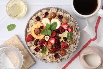 Oatmeal with freeze dried fruits, nuts and mint on white tiled table, flat lay