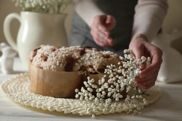 Woman decorating delicious Italian Easter dove cake (traditional Colomba di Pasqua) with flowers at white wooden table, closeup