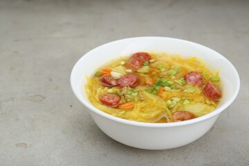 Delicious sauerkraut soup with smoked sausages and green onion on light grey table