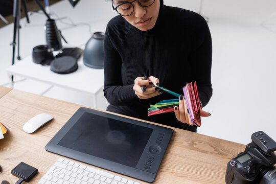african american retoucher choosing color samples near graphic tablet on desk in photo studio.
