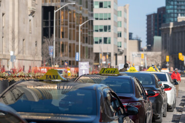 Row of many taxi cars with yellow TAXI signs parked at a busy city street, selective focus....