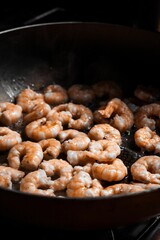 Close-up shot of shrimps being fried in a hot skillet on a stove top