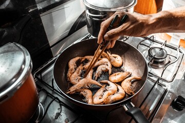 Chef is cooking prawns in a skillet on a gas stove top