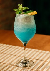 Close-up image of a vibrant blue cocktail with ice in a tall glass, lemon slice as garnish