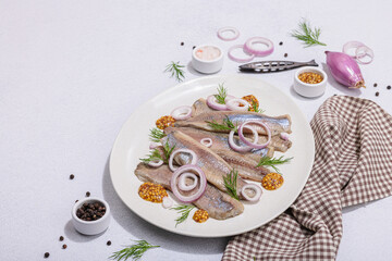 Salted herring with dijon mustard, dill and red onion rings on white stone background