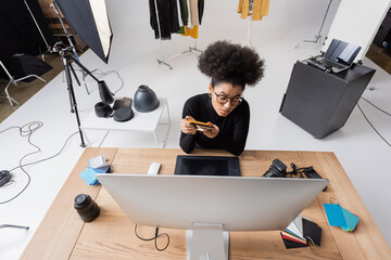high angle view of african american retoucher sitting with color samples near computer and graphic tablet in modern photo studio.