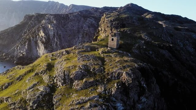 Drone view of the signal tower ruins on the mountain slope on a sunny day on an island in Donegal