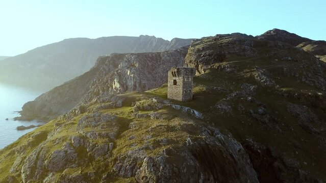Drone view of the signal tower ruins on the mountain slope on a sunny day on an island in Donegal