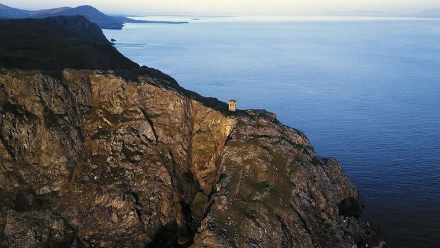 Drone orbit of the signal tower ruins on the mountain slope before the sea on an island in Donegal