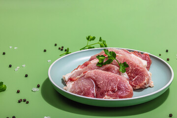 Pieces of pork meat with parsley on gray dish, raw fresh steaks concept. Sea salt, spices
