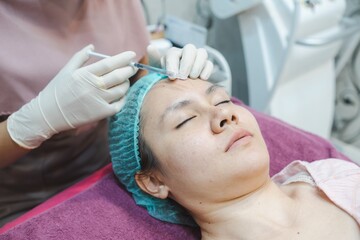 Naklejka premium A nurse injects a skin serum onto the face of an Asian woman. In beauty clinics, Medical and cosmetic dermatology appointments concept.
