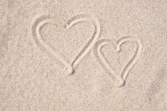 Sand background. Simple image of two hearts drawn on sand. Sandy beach. Blank negative space for copy.
