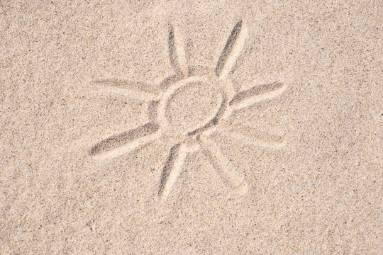 Sand background. Simple image of sun drawn on sand. Sandy beach. Blank negative space for copy.