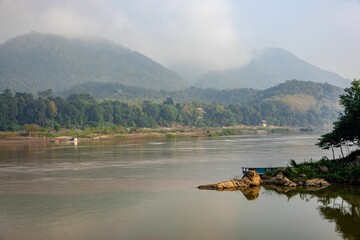 Beautiful shot of the Mekong River with a floating boat near mountains in Luang Prabang, Laos