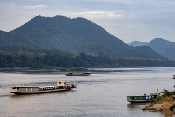 Beautiful shot of the Mekong River with floating boats near mountains in Luang Prabang, Laos