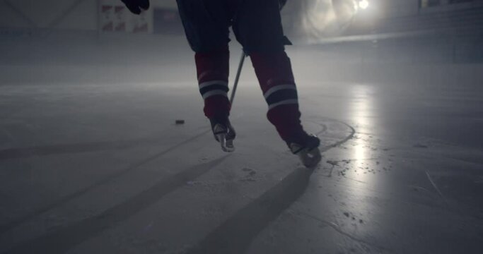 Hockey player in red uniform skating on ice stick handling puck in the dark