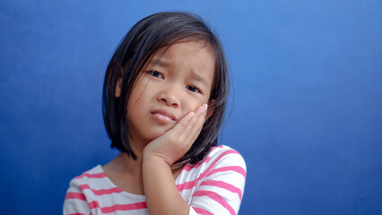 Asian kid girl toothache. Kid suffering from toothache. Asian child hand on cheek face as suffering...