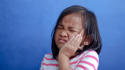 Asian kid girl toothache. Kid suffering from toothache. Asian child hand on cheek face as suffering from facial pain, mumps toothache. Dental health care.
