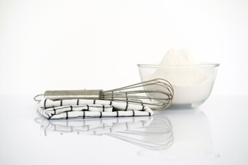Baking concept. Bowl with a whisk and dishcloth on white table over white background with copy space.
