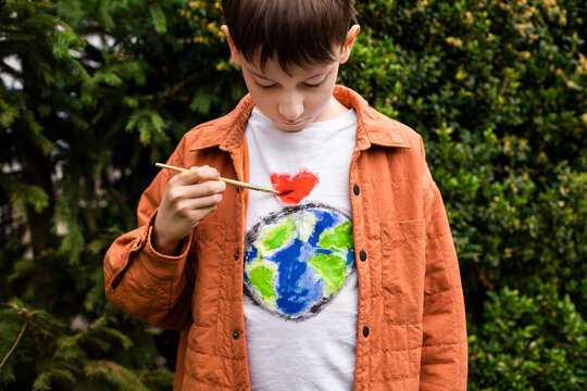 Sustainable lifestyle concept. Schoolboy drawing earth globe on t-shirt. Green energy, ESG, renewable resources, environmental care, protecting planet. 