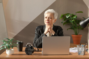 Confident stylish european middle aged senior woman using laptop at workplace. Stylish older mature 60s gray haired lady businesswoman sitting at office table. Boss leader teacher professional worker